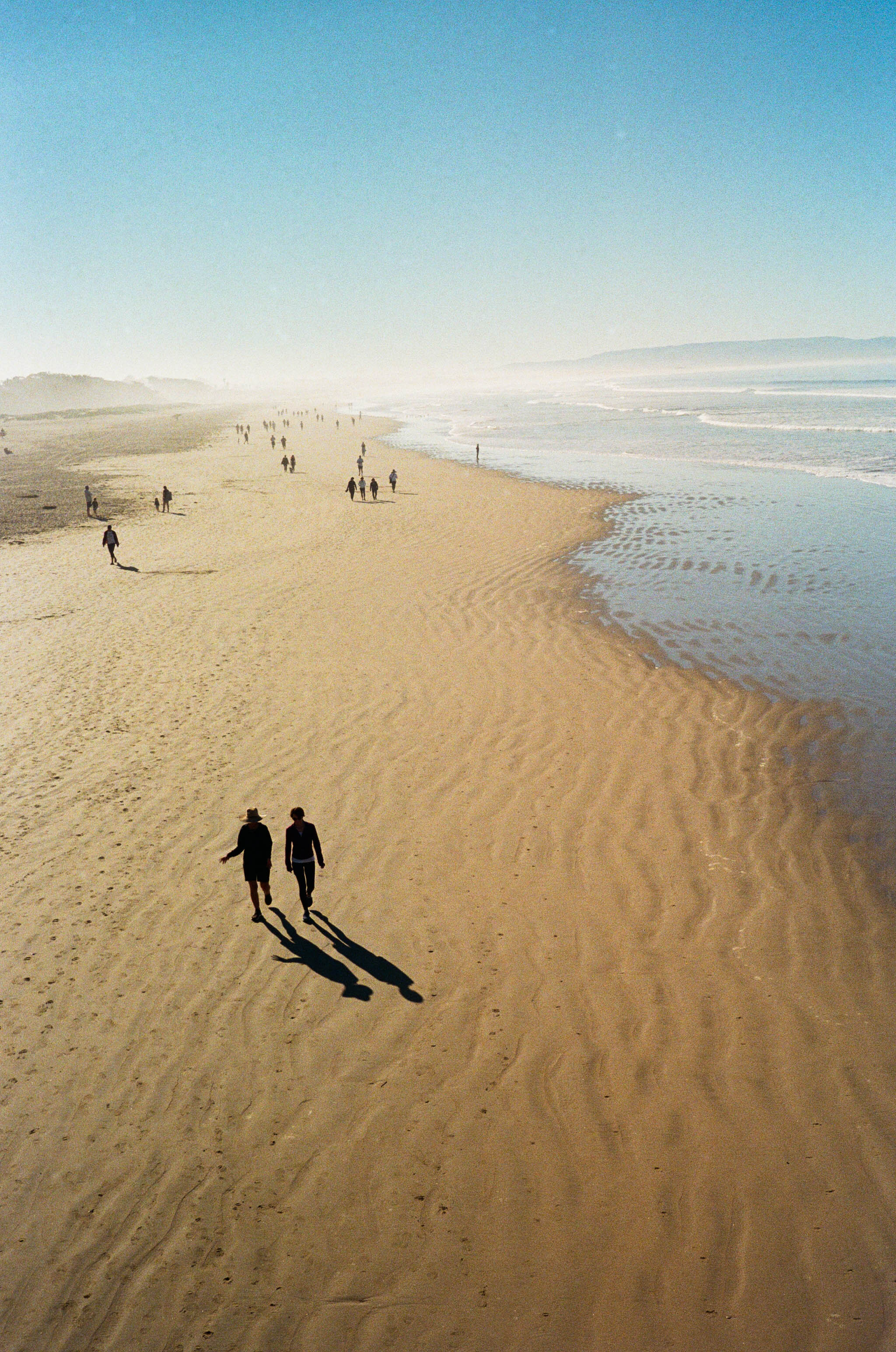Couple walking on beach casting long shadows