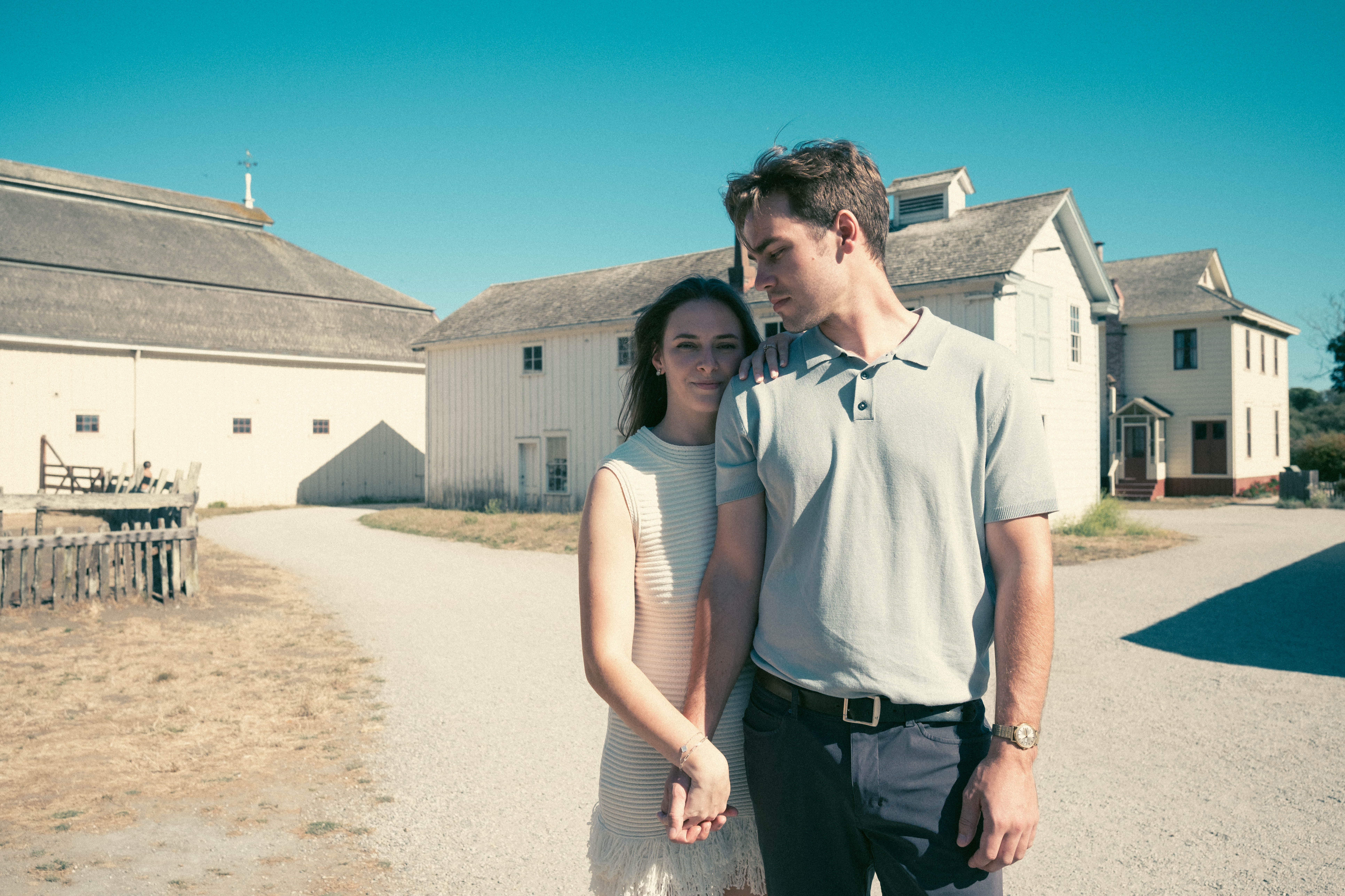 Couple walking together in front of white farm buildings