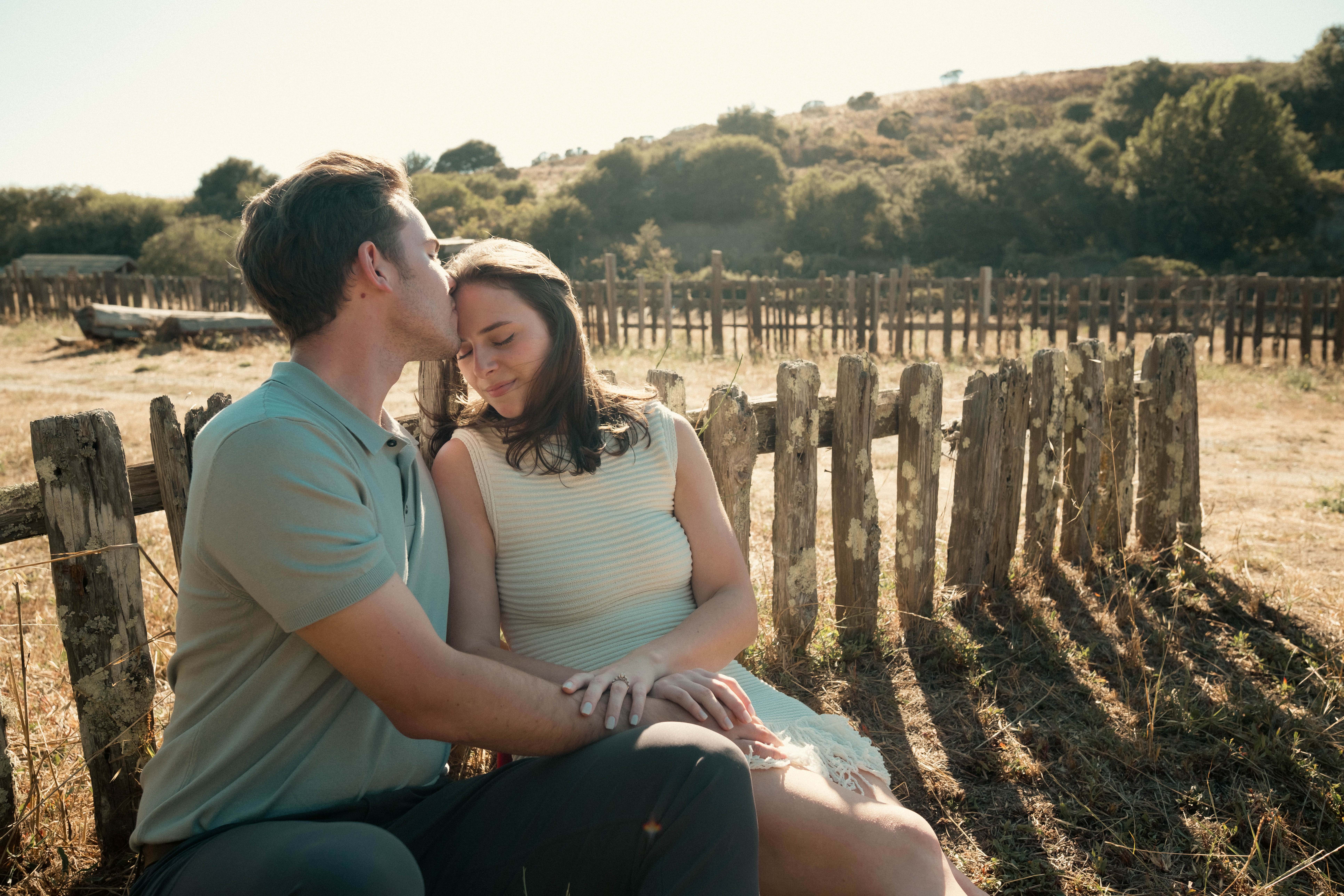 Engagement couple sitting by weathered fence in field