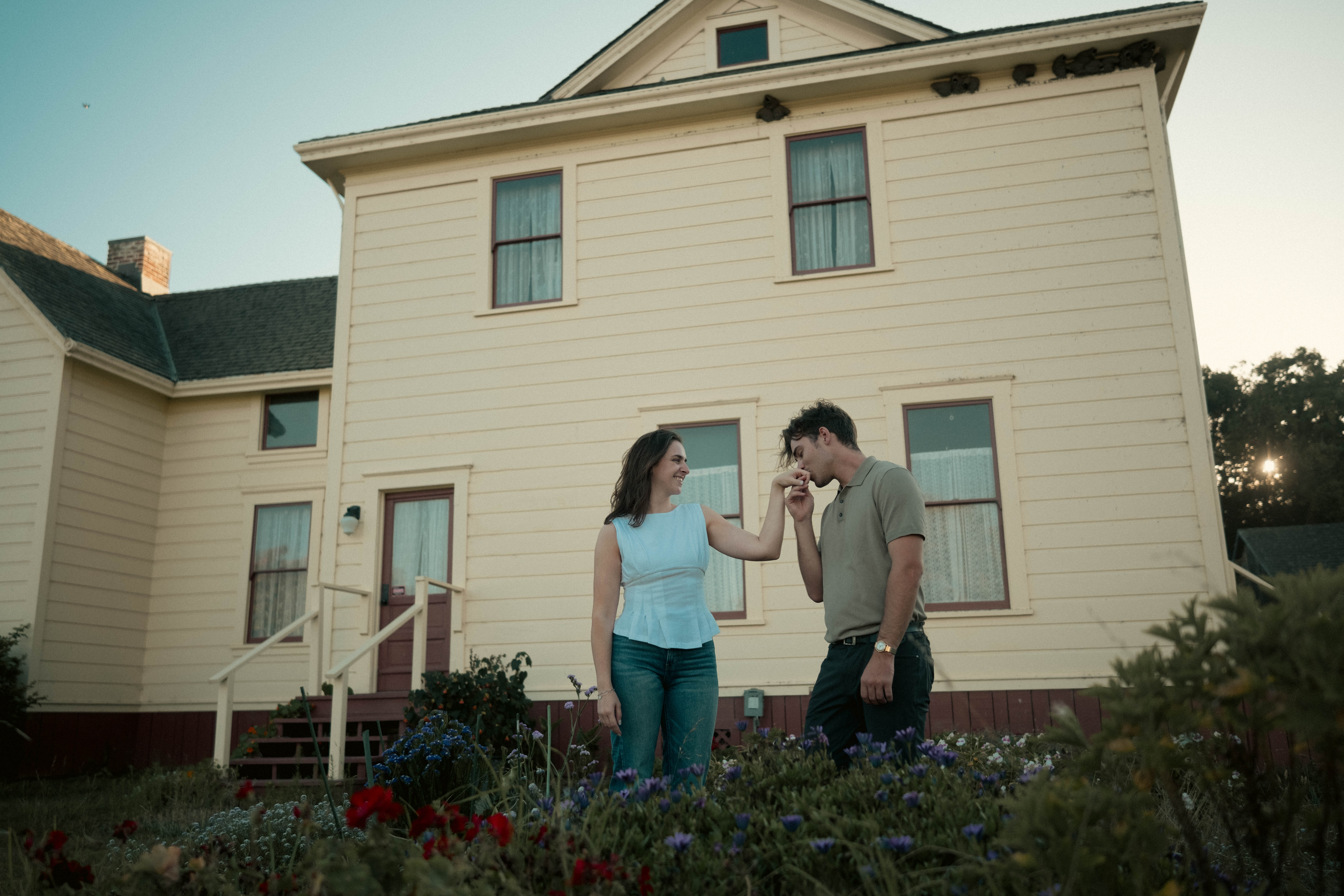 Engagement couple in front of white house with flower garden